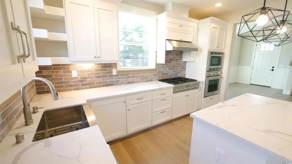 A kitchen designed by Bay Valley Development with white cupboards, marble tops, wood flooring, brick walls and modern lighting.
