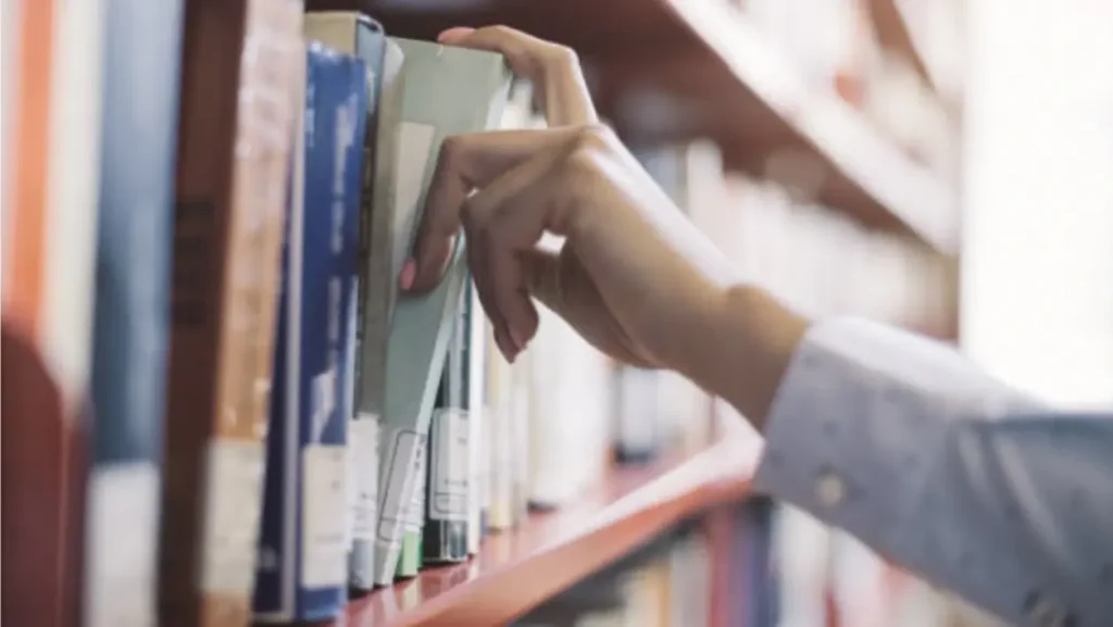A close-up shot shows a person's hand reaching for a book on a wooden bookshelf at Chattleton Place.