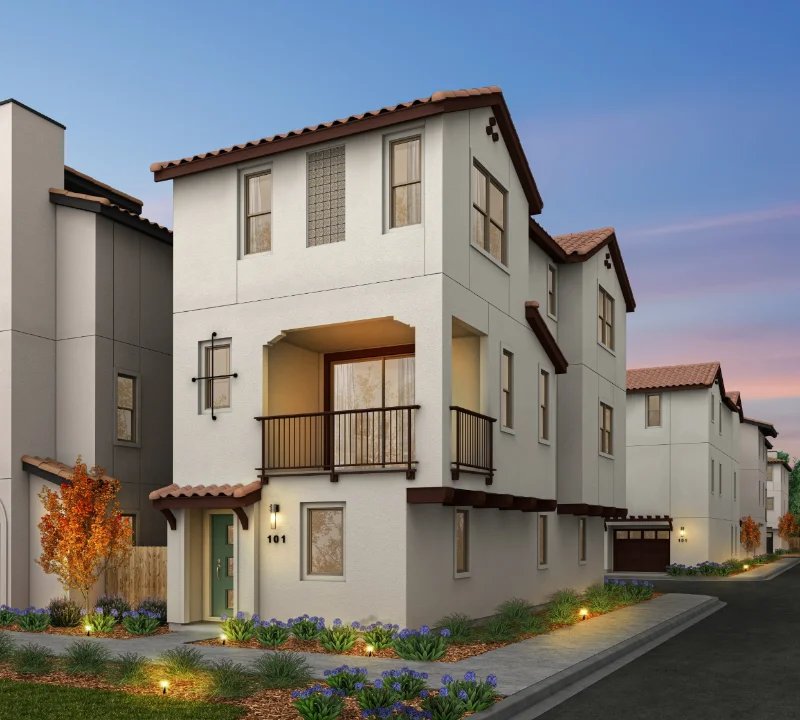 An upscale three-story single-family home at Chattleton Place features a white exterior, brown tile roof, and a second-story balcony, illuminated by dusk lighting and surrounded by landscaped greenery.